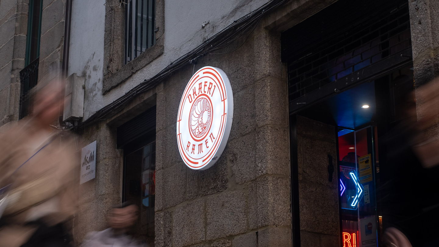 The front of Ramen Okaeri at night, its lit circular sign on the stone wall of Rúa das Orfas