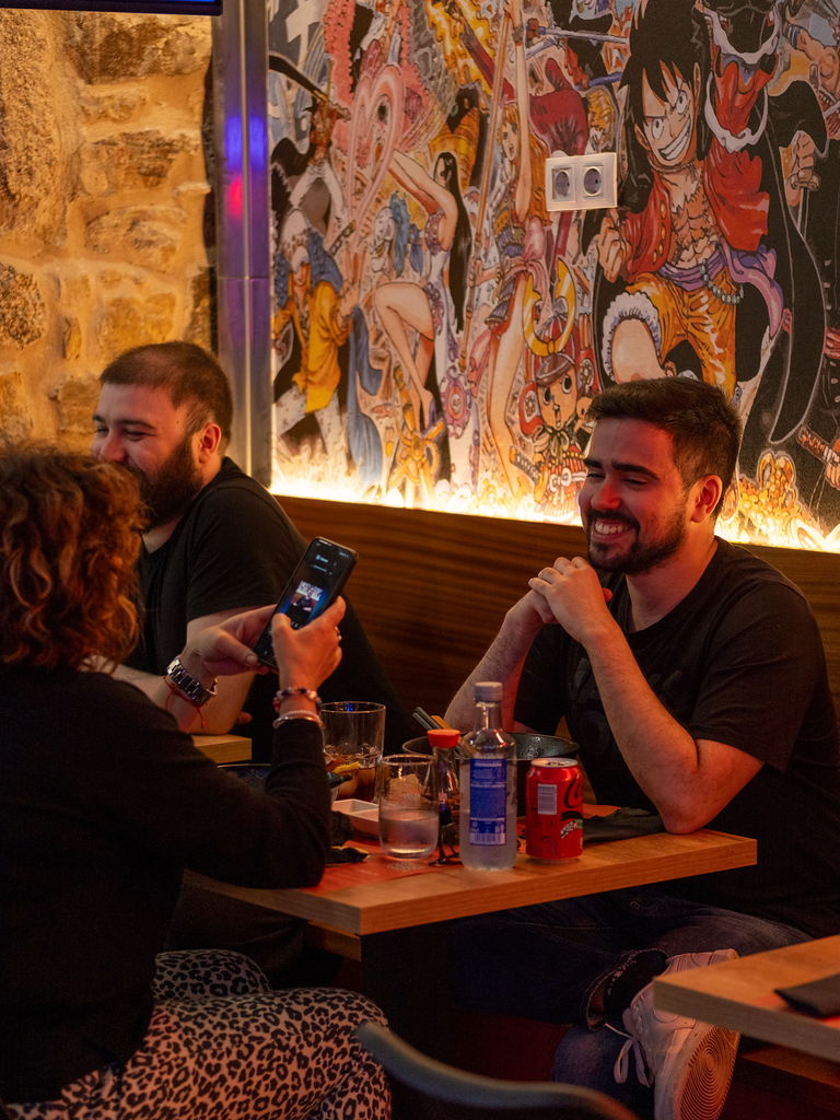 Three people eating and laughing at a table, with a manga mural behind them