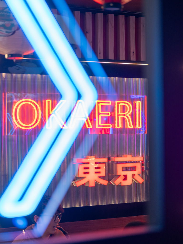 Blue neon arrows in front of the OKAERI sign and the red Tokyo characters