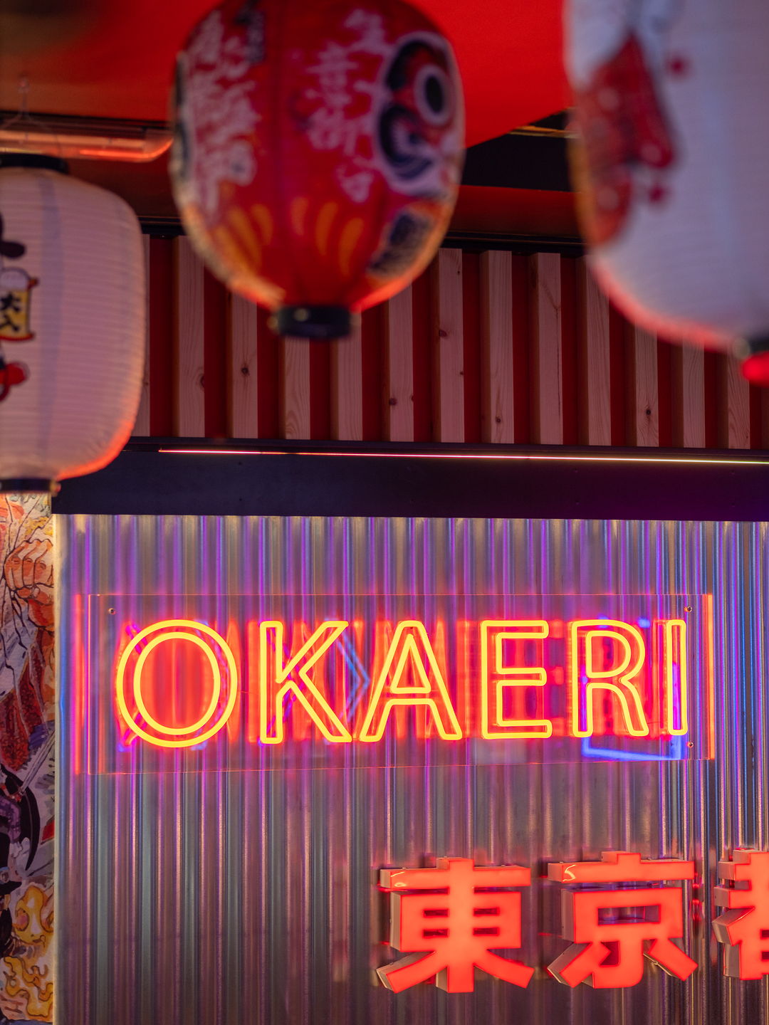A neon sign reading OKAERI, with Japanese lanterns hanging from the ceiling