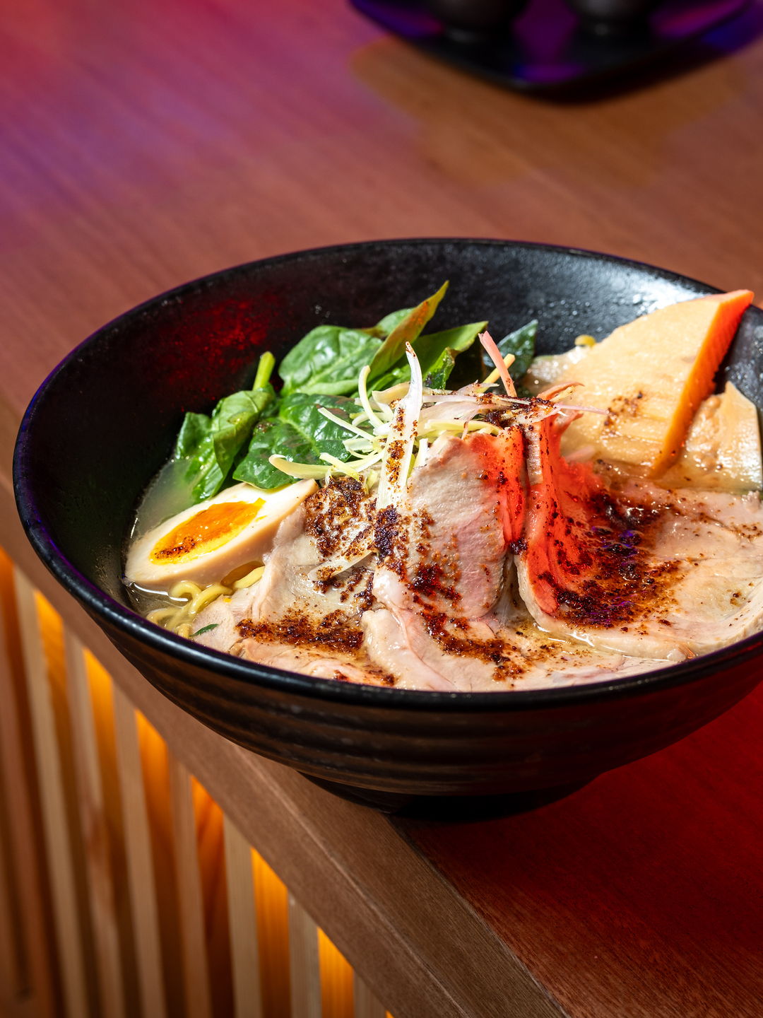 A bowl of ramen with chashu, marinated egg, bamboo and spinach on the wooden counter